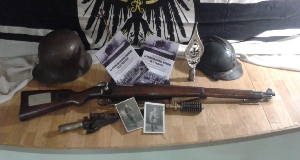 Muestrario con bandera de acorazado alemán, fusil Mauser germano, casco francés, casco prusiano, bayoneta británica, granada y fotografías originales.